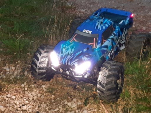 1-10 RC Monstertruck mit LED Lichtband Blaues ferngesteuertes Monstertruck-Modell auf unebenem Gelände.