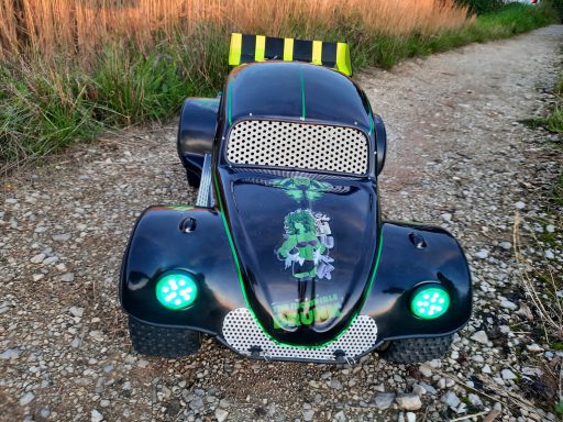 1 zu 5 Beetle mit Beleuchtung und Highpipes Schwarzes beliebtes Spielzeugauto mit grünen Lichtern, auf einem Kiesweg platziert.