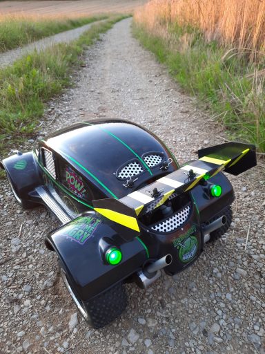 1 zu 5 Beetle mit Beleuchtung und Highpipes Schwarzes Modellauto mit grünen und gelben Akzenten auf einem Kiesweg.
