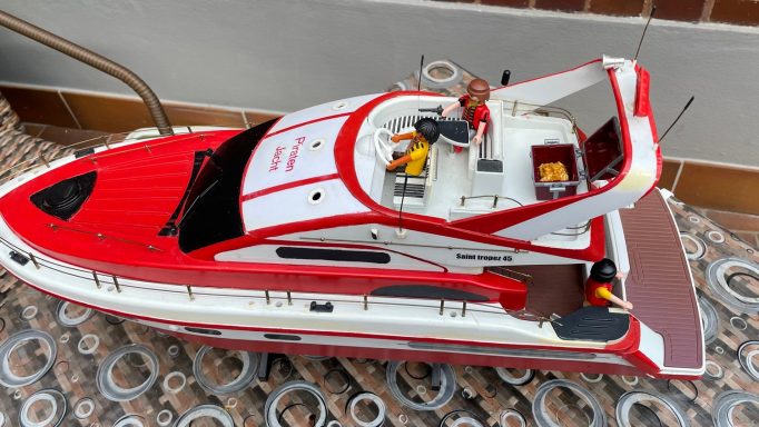 RC St Tropez Jacht umgebaut Rotes Modellboot mit Zubehör auf einem gemusterten Untergrund.